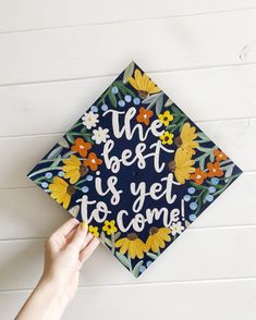 someone holding up a graduation cap that says the best is yet to come