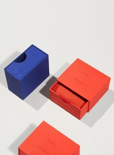 three different colored boxes sitting next to each other on top of a white surface with one open and the other closed