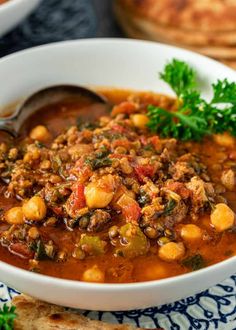 a close up of a bowl of soup on a plate with pita bread in the background