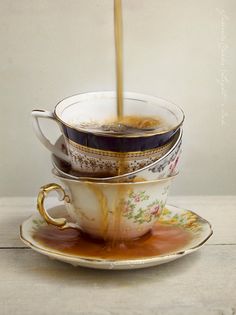 tea being poured into a cup with saucer and plate on the side, sitting on top of each other