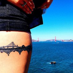 a woman with a tattoo on her thigh looking out at the water and bridge in the distance