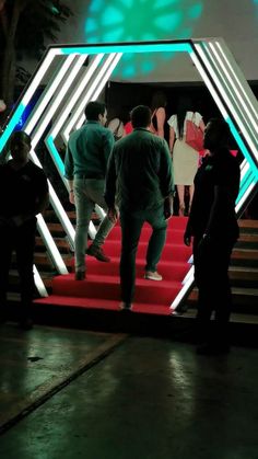 people are walking down the red carpeted stairs in front of a large screen display