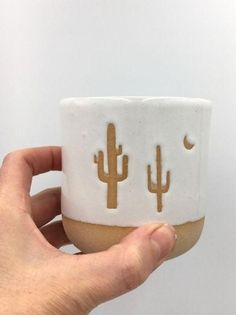 a hand holding a ceramic cup with two cactus designs on it