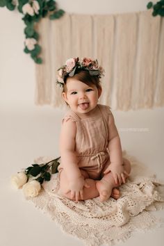 a smiling baby sitting on a blanket with flowers in her hair