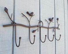 a metal hook with birds on it hanging from the side of a wooden wall next to hooks