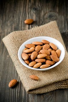 almonds in a white bowl on a burlocked linen napkin with wooden background