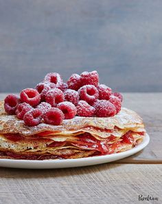 a stack of pancakes covered in raspberries on top of a white plate with powdered sugar