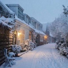 a snow covered street lined with houses and parked bicycles in front of the house at night