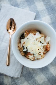 a white bowl filled with food next to a spoon and napkin on top of a checkered table cloth