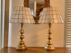 two lamps sitting on top of a wooden table next to a mirror and lamp shade