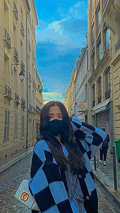 a woman wearing a black and white checkered coat is standing in an alley way