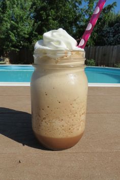 a drink with whipped cream and a pink straw in a mason jar next to a swimming pool