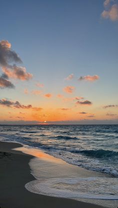 the sun is setting over the ocean with clouds in the sky and waves on the beach