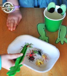 a child is playing with some fake bugs on the table next to a green cup