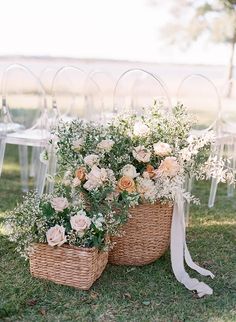 two wicker baskets filled with flowers and greenery on the grass under clear acrylic chairs