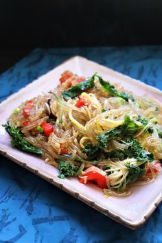 a plate full of noodles and vegetables on a blue tablecloth