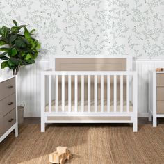 a baby crib in the corner of a room with two dressers and a potted plant