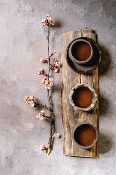 two cups of tea sit on a wooden tray next to a branch with flowers in it