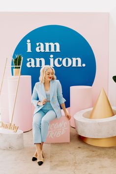 a woman sitting on top of a pink chair next to a sign that says i am an icon