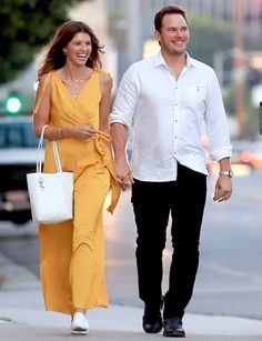 a man and woman are walking down the street holding hands as they smile at each other