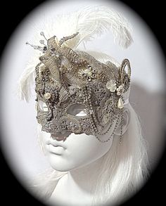 This opulent masquerade mask is platinum silver with lace overlays and gorgeous vintage rhinestone appliques that surround the top and cheeks. A vintage jewelry piece and a silver beaded flower are center on the forehead. The molded mask is loaded with rhinestones, gems, and vintage bead accents. Pearl drops & loops of rhinestone chain add elegant touches to this Art Deco style mask. Sprays of white ostrich feathers frame the top and one ear. It ties with white satin ribbons in back and is f Silver Rhinestone Eye Masquerade Mask, Silver Rhinestone Eye Mask For Masquerade, Elegant Silver Eye Mask, Silver Masquerade Mask With Rhinestones For Costume Party, Silver Rhinestone Masquerade Mask For Costume Party, Vintage Masquerade Mask For Carnival, Vintage Masquerade Mask For Carnival Party, Wedding Masquerade Mask With Rhinestones, Elegant Silver Masks And Prosthetics For Party