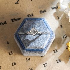 an engagement ring sits in a blue velvet box next to white flowers on a table