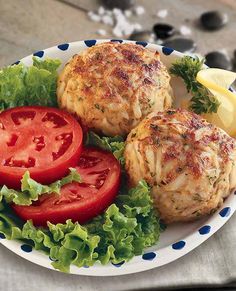 two crab cakes with tomatoes and lettuce on a plate next to lemon wedges