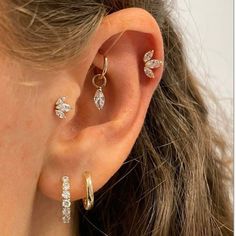 a woman wearing three different types of ear piercings in gold and silver, both with leaves on them