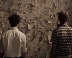 two people standing in front of a wall covered with papers