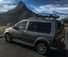 an suv parked in front of a mountain with a surfboard on the roof rack