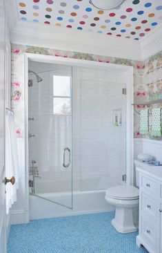 a bathroom with polka dot wallpaper and blue floor tiles on the walls, along with a walk in shower