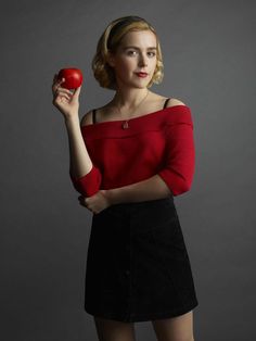 a woman is holding an apple and posing for a photo in front of a gray background