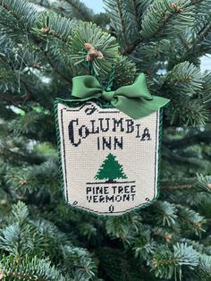 a christmas ornament hanging from the top of a pine tree with green ribbon