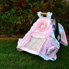 a baby stroller covered in pink and blue blankets sitting on the grass next to bushes