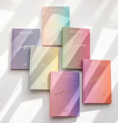 five different colored notebooks sitting next to each other on top of a white surface