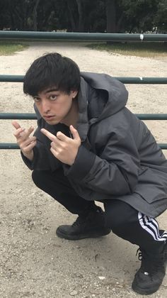 a young man kneeling down in front of a metal fence with his hand on the ground