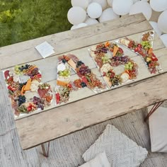 a wooden table topped with lots of different types of food next to white balloons in the background