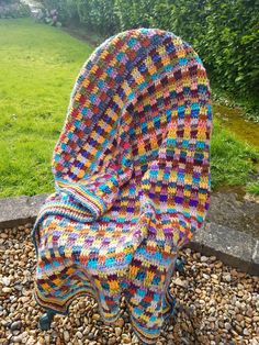 a crocheted chair sitting on top of gravel covered ground next to a lush green field