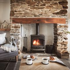 two cups of coffee sit on the table in front of an open fire place with a wood burning stove