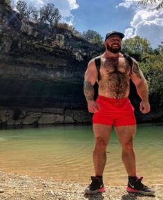 a man standing in front of a body of water wearing red shorts and a black hat