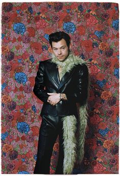 a man in a black suit and fur stoler posing for a photo against a floral wall