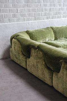 a green couch sitting in front of a white brick wall with no one on it