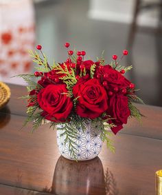 a bouquet of red roses in a white vase on a table next to a candle