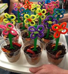 there are many cups with flowers in them on the tray and people standing behind it