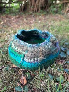 there is a crocheted pot on the ground in the grass with leaves around it