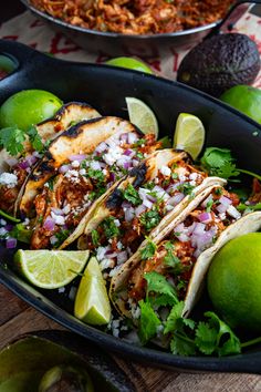 three tacos with limes, onions and cilantro on a wooden table