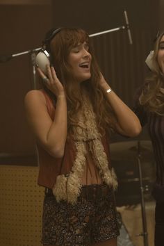 two young women singing into headphones in a recording studio, one holding a microphone and the other listening to music