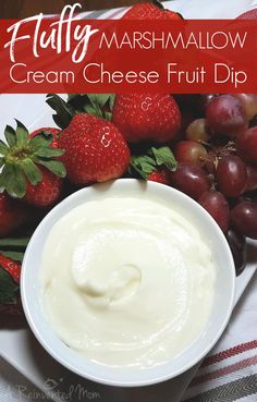 a bowl of cream cheese fruit dip surrounded by strawberries and grapes on a white plate