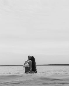 a woman sitting in the water with her arms around her neck, looking up into the sky