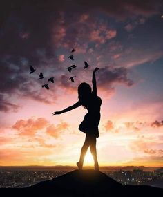 a woman standing on top of a hill with birds flying in the air